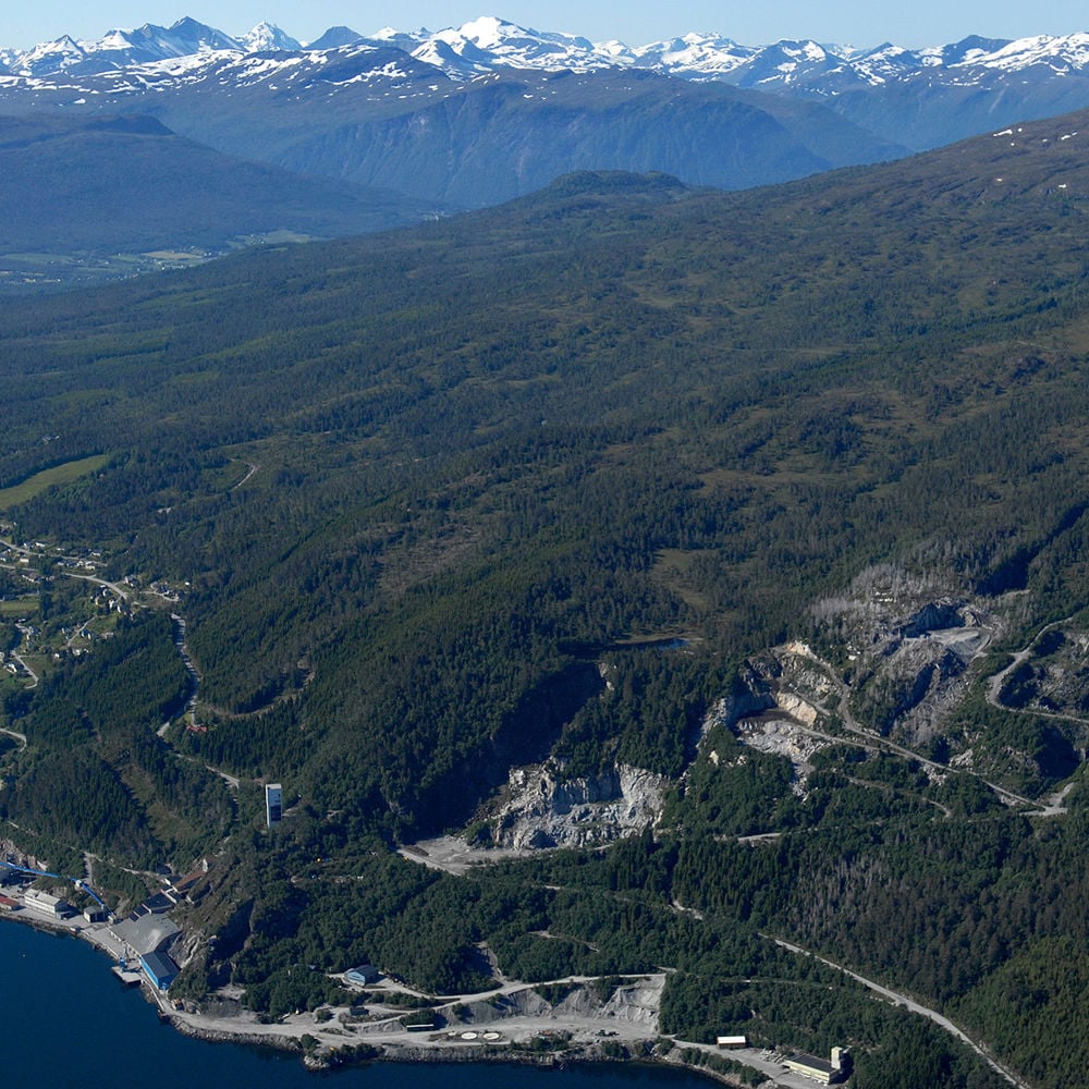 Flyfoto med utsikt over fjord og fjell. Massemottak i åsside. Foto.