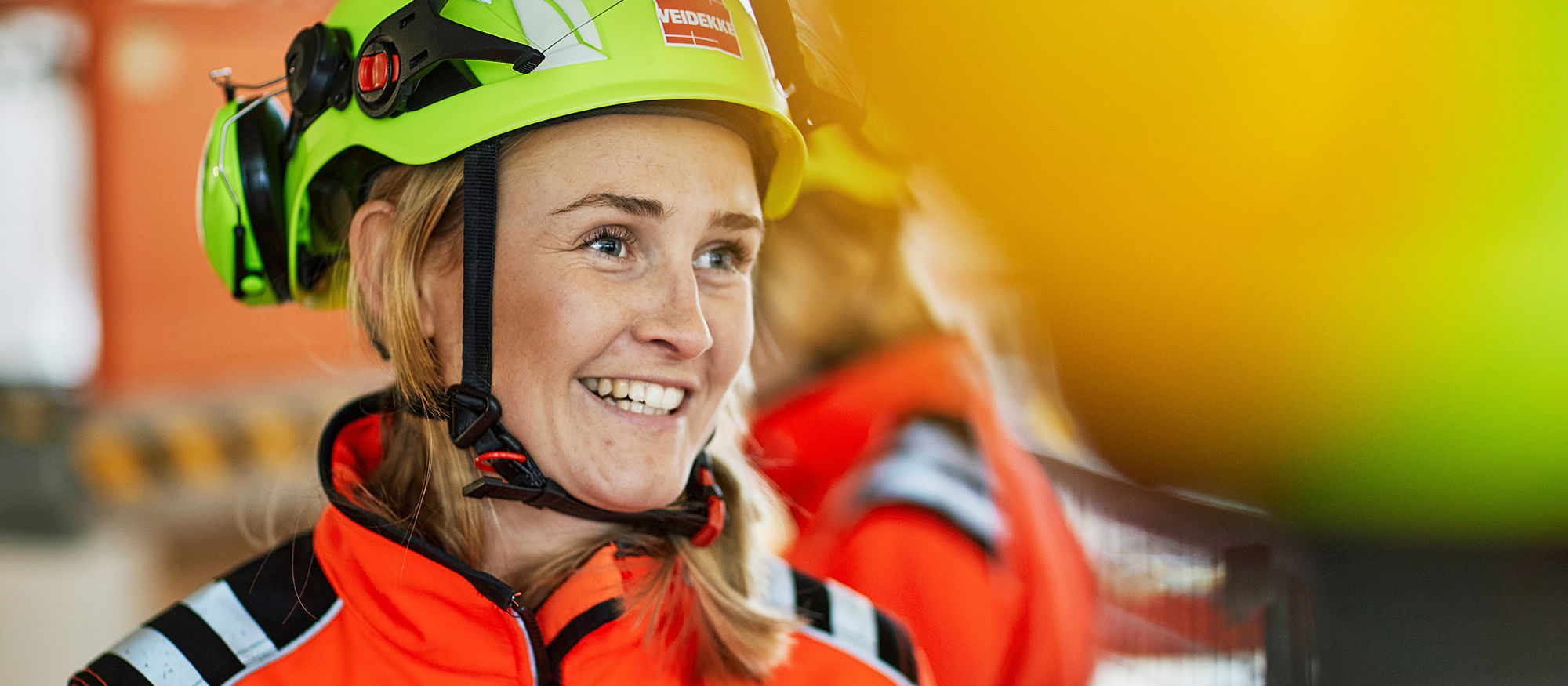 Kvinne på byggeplass, smilende ser til siden.